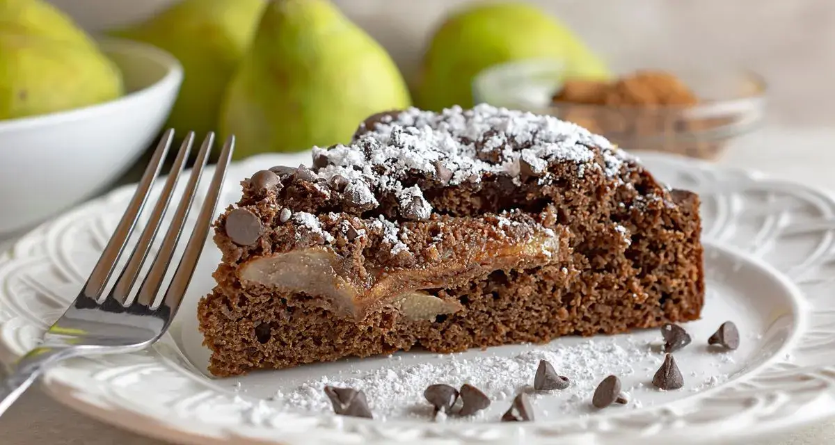 Una fetta di torta pere e cioccolato, cosparsa di zucchero a velo e gocce di cioccolato, con pere caramellate all'interno.