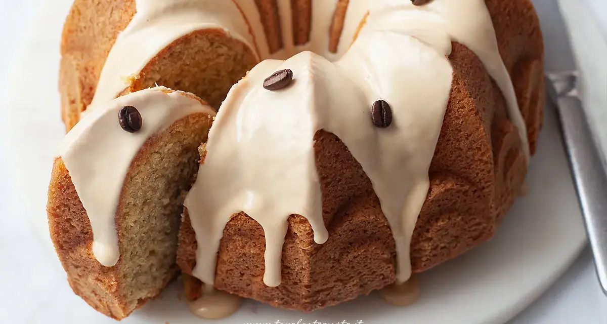 Torta al caffè soffice e profumata, ricoperta da una glassa chiara e decorata con chicchi di caffè. Una fetta è stata tagliata, rivelando l'interno morbido.