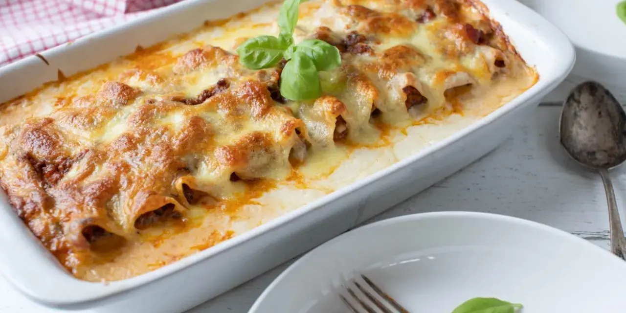 Cannelloni ripieni di carne macinata e mozzarella, cotti al forno e gratinati, con una foglia di basilico fresco.