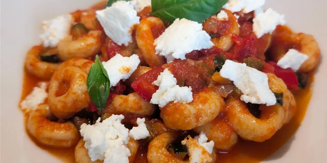 Anellini alla pecorara con pomodoro, zucchine e ricotta fresca, guarniti con foglie di basilico.