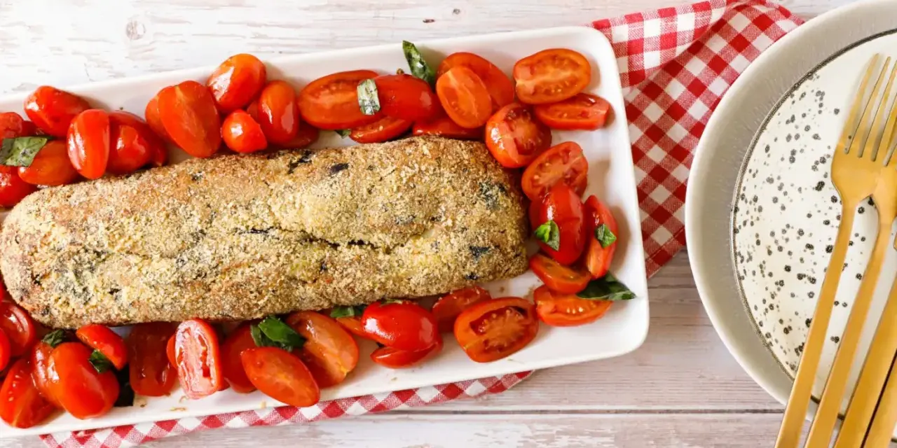 Polpettone di melanzane dorato e croccante, circondato da pomodorini freschi e basilico, pronto per essere gustato.