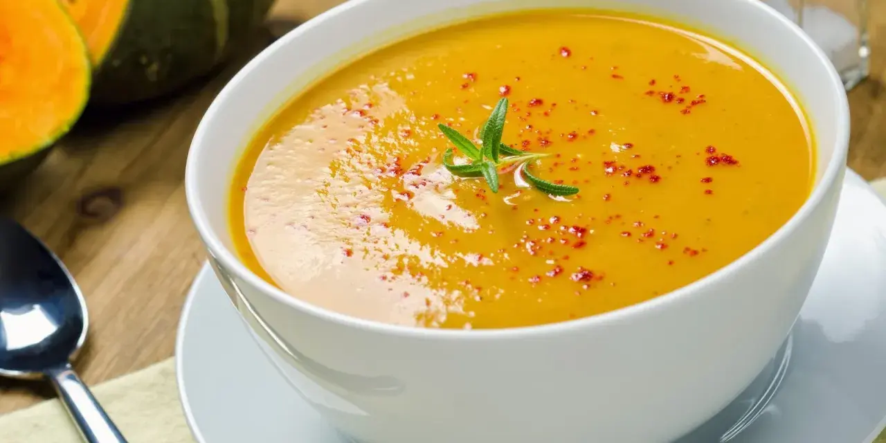 Una cremosa vellutata di zucca, guarnita con rosmarino e paprika, pronta per essere gustata.