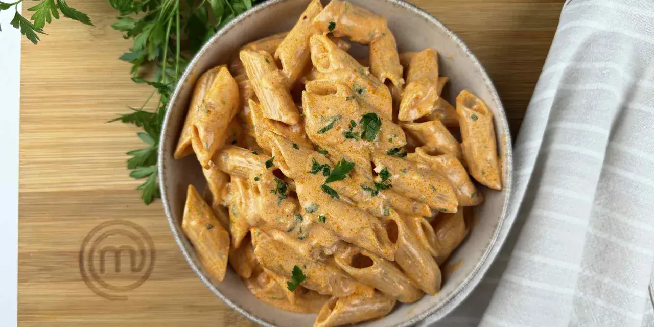 Penne alla vodka cremose e invitanti, guarnite con prezzemolo fresco, su un tagliere di legno con il logo di MasterChef.