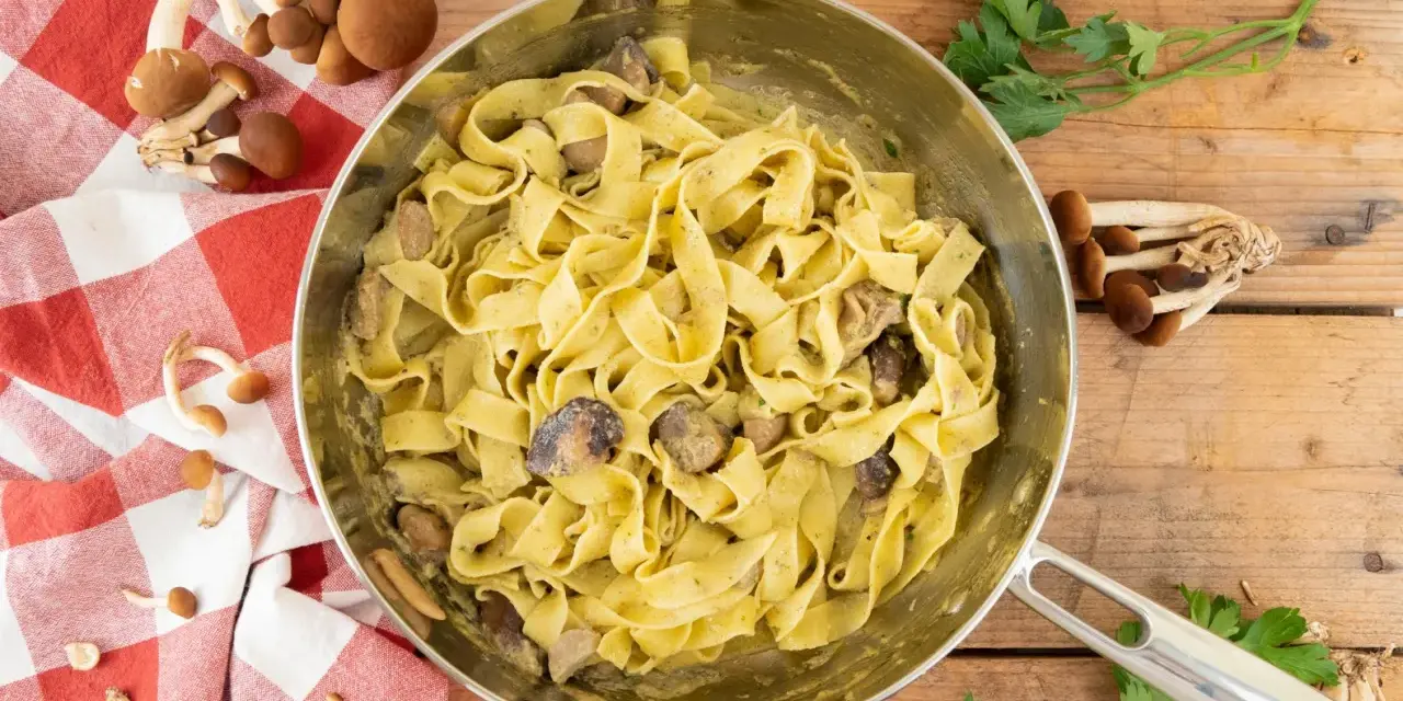 Tagliatelle ai funghi cremose in padella, con funghi freschi e prezzemolo su fondo di legno.