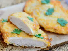 Deliziose cotolette di pollo dorate, tagliate a metà per mostrare la succosa carne bianca, guarnite con prezzemolo fresco.