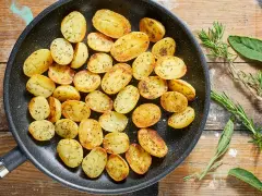 Patate novelle dorate e profumate in padella, condite con erbe aromatiche fresche, pronte per essere gustate.