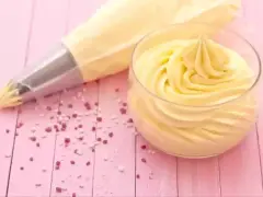 Sac à poche con crema al burro pronta per decorare, accanto a un bicchiere colmo della stessa soffice crema.