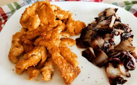 Straccetti di pollo al forno dorati e croccanti, serviti con radicchio stufato. Un piatto semplice e gustoso.
