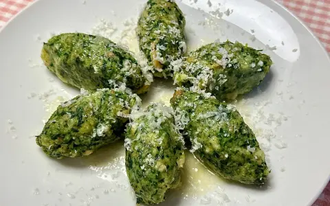 Strangolapreti alla trentina, verdi e saporiti, spolverati di formaggio grattugiato su un piatto bianco.
