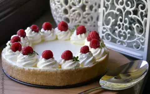 Cheesecake senza gelatina decorata con panna montata e lamponi freschi, pronta per essere servita.