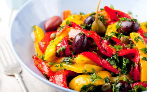 Peperonata ricetta della nonna: un piatto colorato con peperoni rossi e gialli, olive, capperi e prezzemolo fresco.