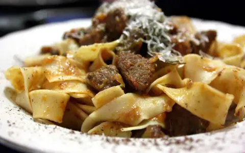 Pappardelle al cinghiale fumanti, con pezzi di carne succulenta e una spolverata di parmigiano.
