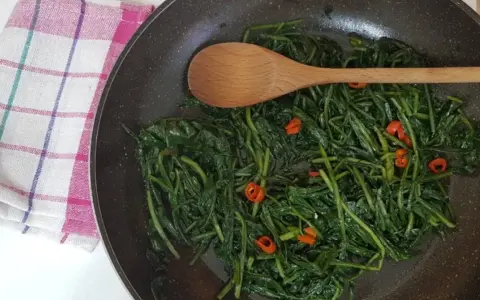 Cicoria in padella con peperoncino, un contorno saporito e salutare. Un cucchiaio di legno mescola le foglie verdi.