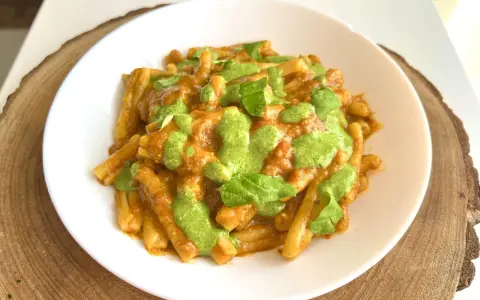Un piatto di pasta alla Portofino, con un sugo rosso e un pesto verde brillante, guarnito con foglie di basilico fresco.