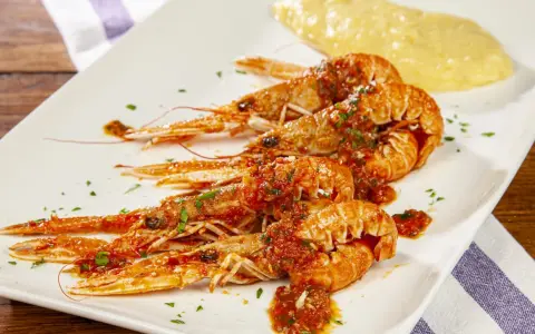 Scampi alla busara succulenti su piatto bianco, con un contorno di polenta gialla.