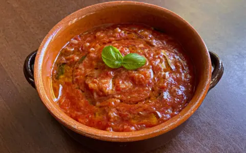 Piatto di pappa al pomodoro in terracotta, guarnito con basilico fresco. Un classico della cucina toscana.