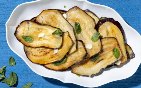 Fette di melanzane grigliate, guarnite con menta fresca e aglio, un contorno di verdure saporito.