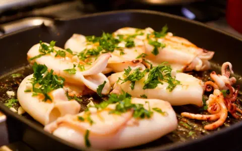Seppie alla griglia succulente, cosparse di prezzemolo fresco, cuociono in una padella scanalata, pronte per essere gustate.