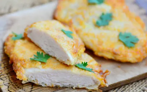 Deliziose cotolette di pollo dorate, tagliate a metà per mostrare la succosa carne bianca, guarnite con prezzemolo fresco.