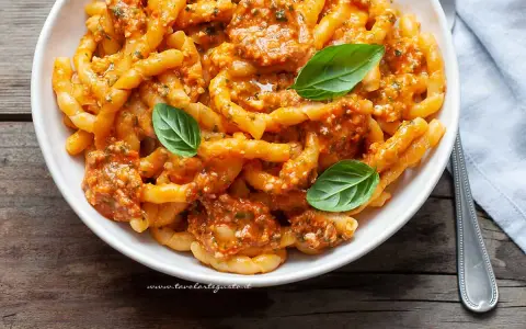 Busiate alla trapanese, un piatto di pasta siciliana con un ricco sugo rosso, guarnito con basilico fresco.