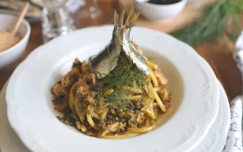 Un piatto di pasta con le sarde, guarnito con finocchietto fresco e due pesciolini interi. Un classico siciliano pronto da gustare.