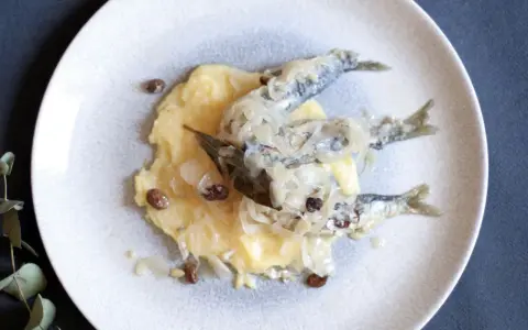 Sarde in saor su un letto di polenta, con cipolle caramellate e uvetta. Un classico veneto.