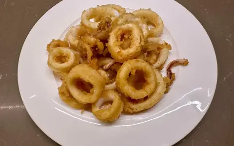 Un piatto bianco pieno di frittura di calamari dorata e croccante, un antipasto invitante.