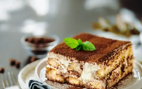 Una fetta di tiramisù ricetta originale, cosparso di cacao e decorato con menta fresca.