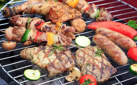 Grigliata di Ferragosto con spiedini, salsicce, bistecche, verdure e pomodori che cuociono sulla brace.
