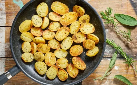 Patate novelle dorate e profumate in padella, condite con erbe aromatiche fresche, pronte per essere gustate.