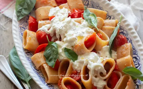 Piatto di pasta con pomodorini e abbondante stracciatella cremosa, guarnito con basilico fresco.