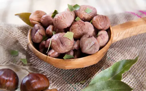 Un cucchiaio di legno trabocca di castagne bollite con buccia, guarnite con foglie verdi. Un assaggio autunnale.
