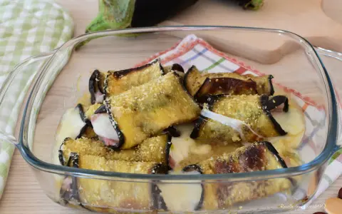 Involtini di melanzane alla siciliana appena sfornati, filanti e dorati, in una pirofila di vetro.
