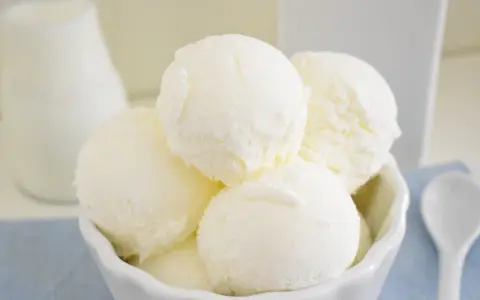 Coppa di gelato cremoso, risultato di una perfetta ricetta gelato con gelatiera. Latte fresco e cucchiaino bianco.