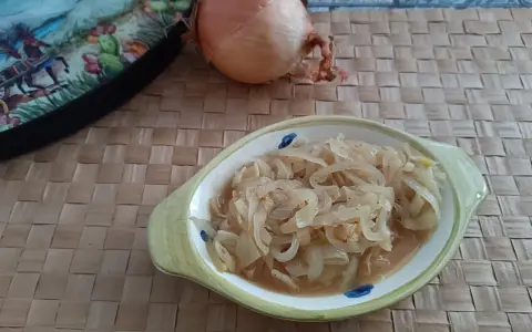 Ciotola con cipolle in agrodolce, accanto una cipolla intera e un piatto decorato.