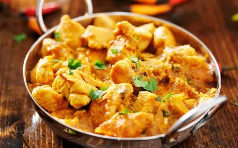 Bocconcini di pollo al curry, un piatto speziato e profumato, servito in una ciotola metallica su un tavolo di legno.