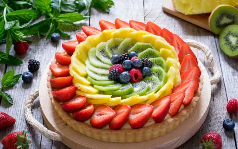 Una colorata crostata di frutta, con fragole, kiwi, ananas e frutti di bosco, su un tavolo di legno rustico.