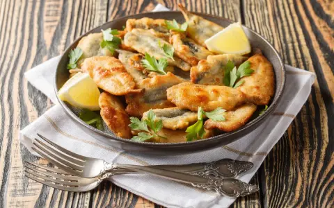 Piatto di acciughe ripiene alla ligure, dorate e croccanti, guarnite con prezzemolo fresco e spicchi di limone.