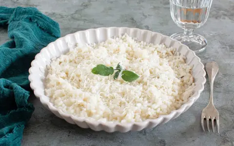 Piatto di riso in cagnone, cremoso e invitante, guarnito con foglie di salvia e parmigiano grattugiato.