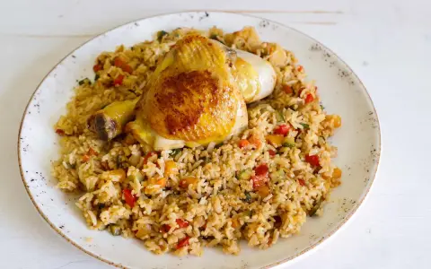 Fusi di pollo in padella serviti su un letto di riso saltato con verdure colorate.