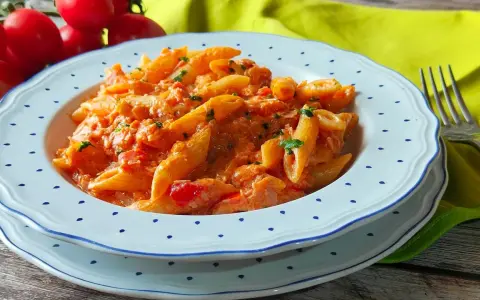 Piatto di penne al baffo cremose, con pomodorini freschi e prezzemolo tritato, servite su un piatto bianco con bordi blu.