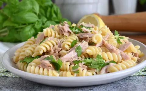 Un piatto di pasta fredda tonno, con fusilli, tonno sfilacciato, prezzemolo fresco e scorza di limone. Perfetta per un pranzo estivo.