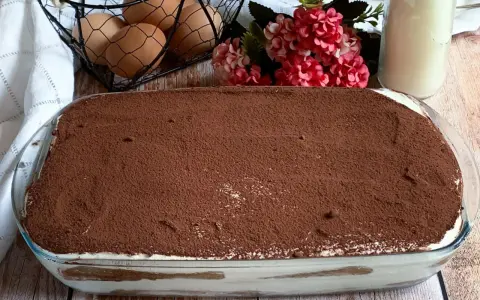 Un invitante tiramisù con panna, cosparso di cacao, pronto per essere gustato. Ingredienti freschi come uova e latte completano la scena.