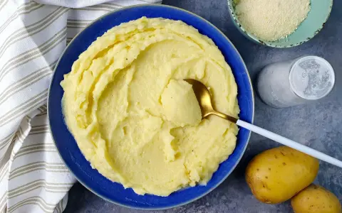 Un piatto invitante di puro di patate cremoso, pronto per essere gustato. Accanto, patate fresche, sale e formaggio grattugiato.