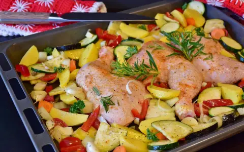 Sovracosce di pollo al forno con patate, zucchine, peperoni e rosmarino, pronte per essere infornate.
