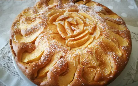 Deliziosa torta di mele senza glutine, con mele disposte a rosa al centro e spolverata di zucchero a velo.