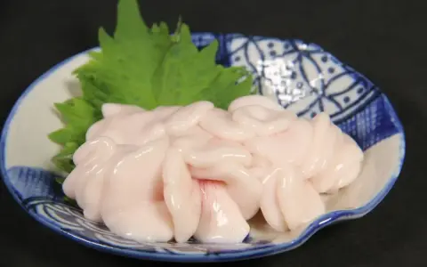 Piatto di lattume di tonno, delicato e rosato, guarnito con una foglia verde su un piatto decorato.