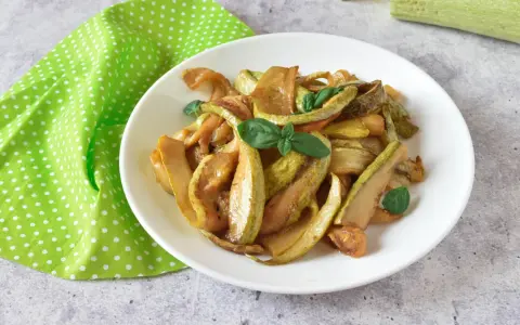 Zucchine in agrodolce, un piatto colorato e saporito, guarnito con basilico fresco su un piatto bianco, accanto a un tovagliolo a pois verdi.
