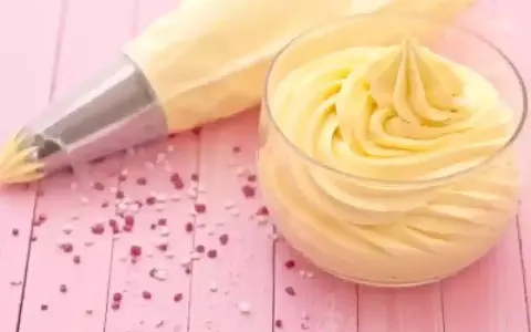 Sac à poche con crema al burro pronta per decorare, accanto a un bicchiere colmo della stessa soffice crema.