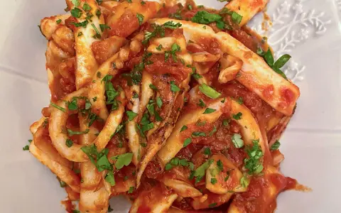 Un piatto invitante di calamari in umido, conditi con una ricca salsa al pomodoro e prezzemolo fresco tritato.